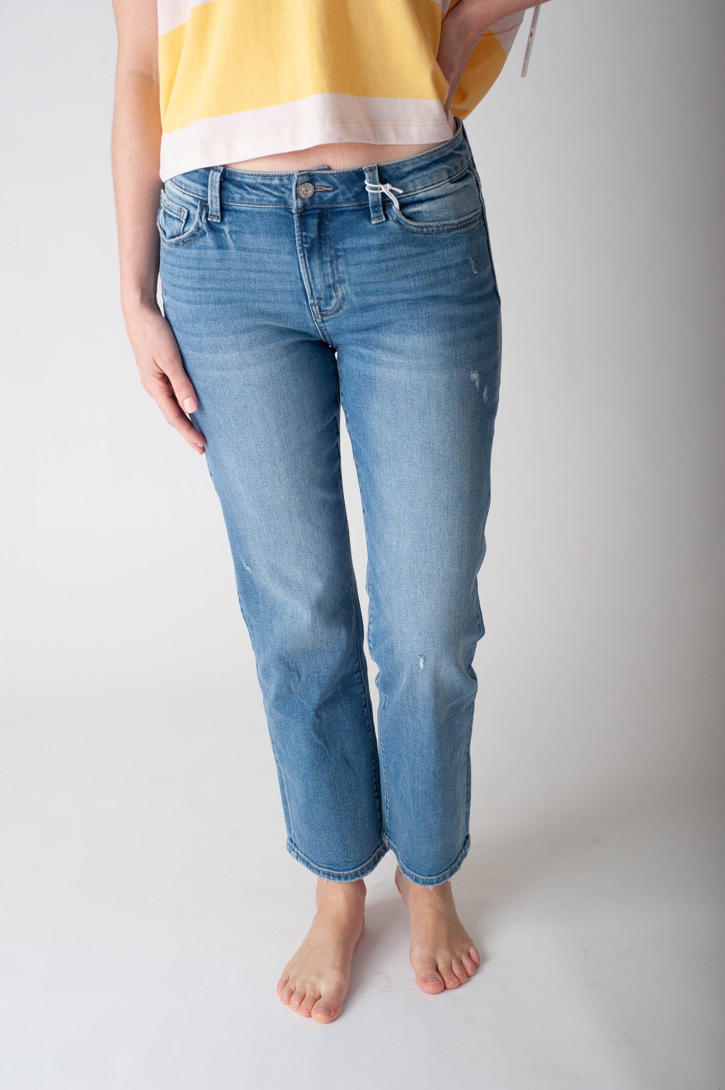 Person wearing blue jeans and a yellow top on a plain background