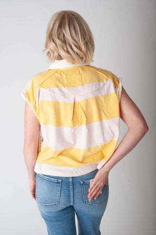 Person wearing a yellow and white striped shirt with blue jeans on a plain background