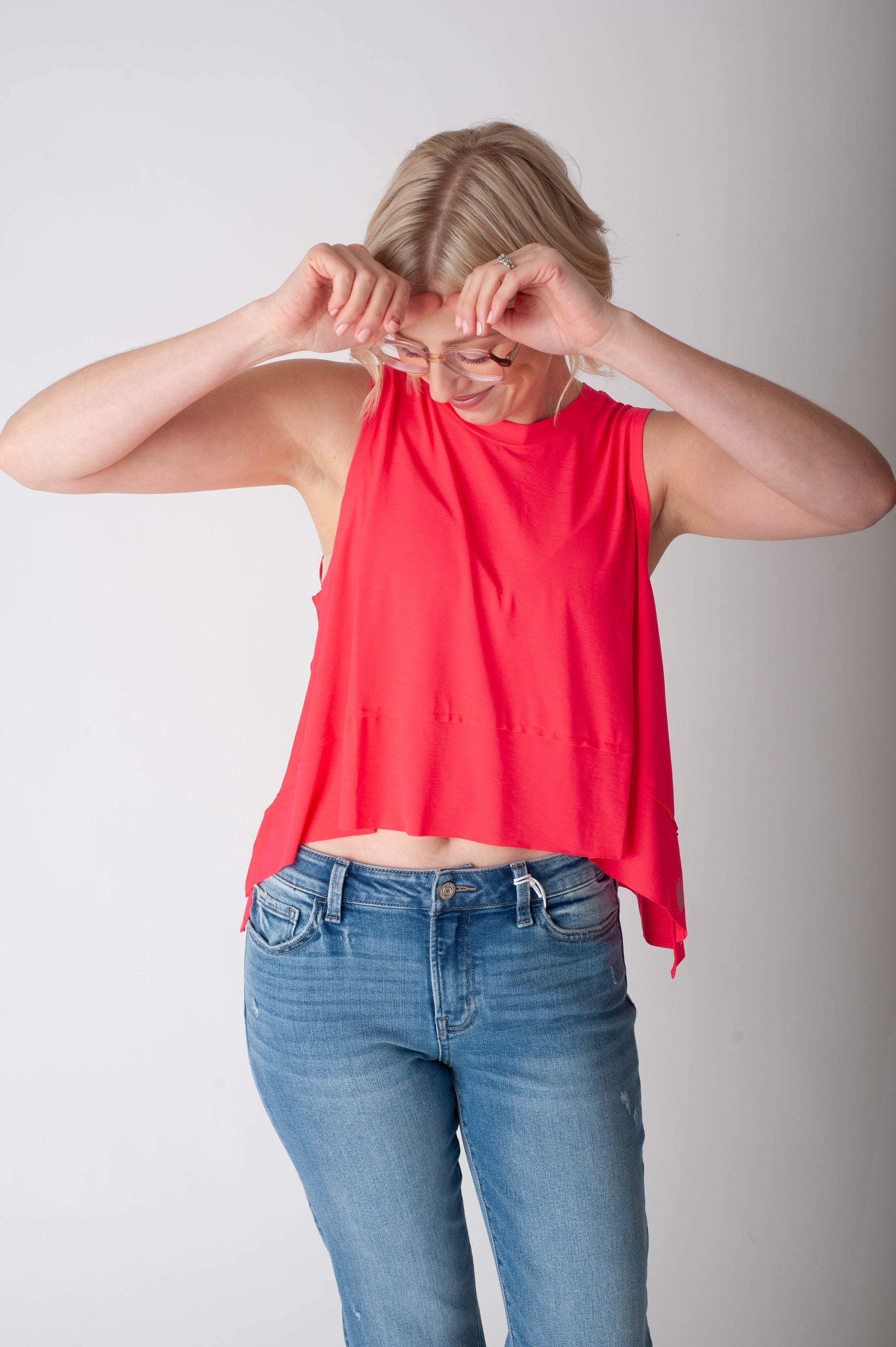 Person wearing a red sleeveless top and blue jeans against a plain background