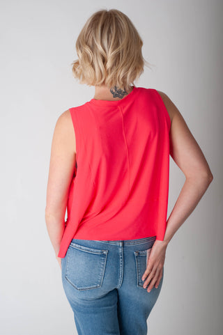 Person wearing a red sleeveless top and blue jeans on a plain background