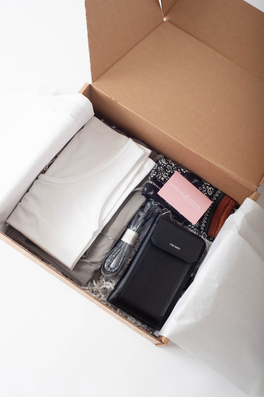 Open cardboard box containing various items including a black wallet, pink notebook, and other small objects on a white background.