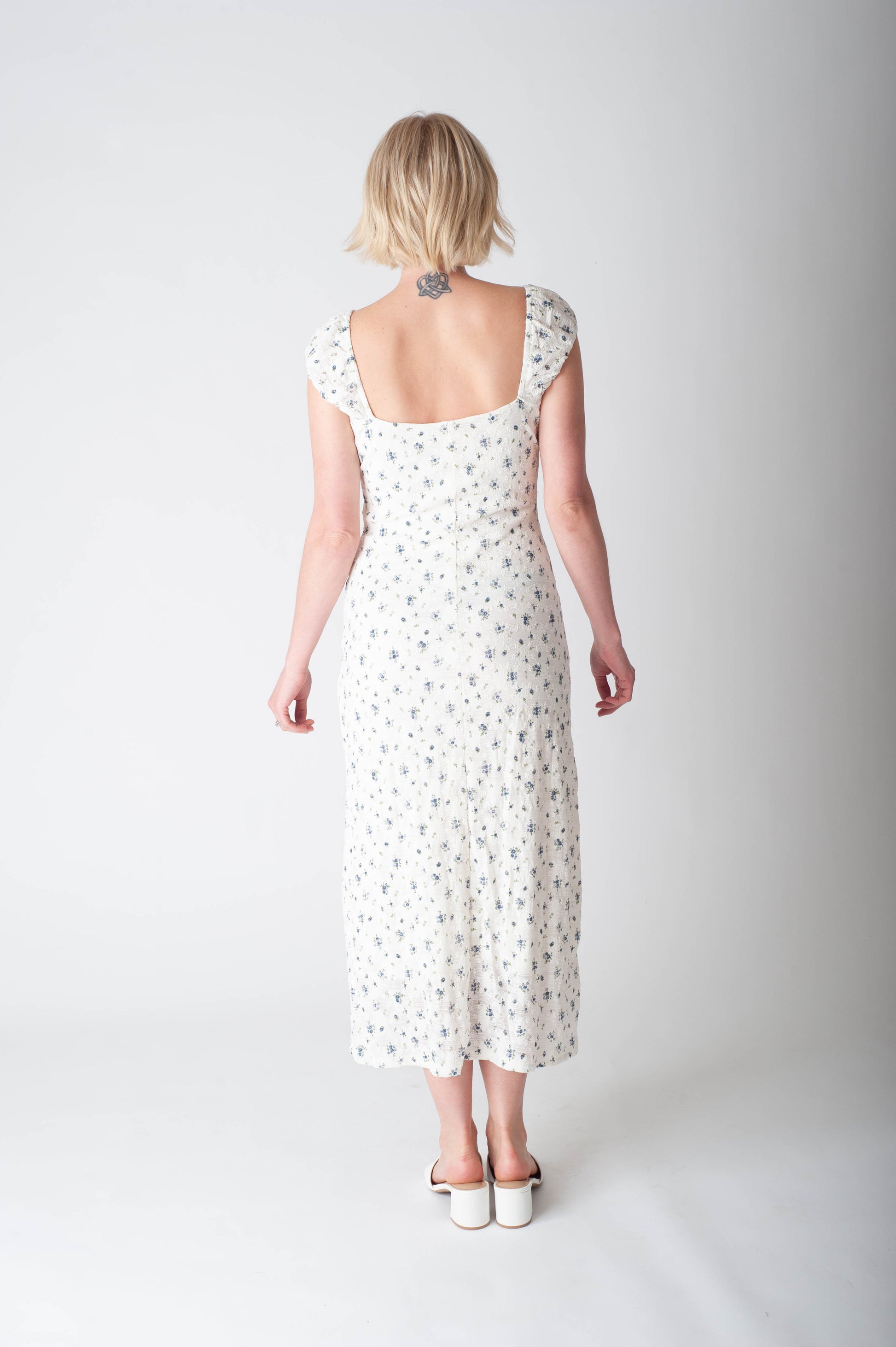 Woman wearing a white dress with a subtle pattern on a plain background