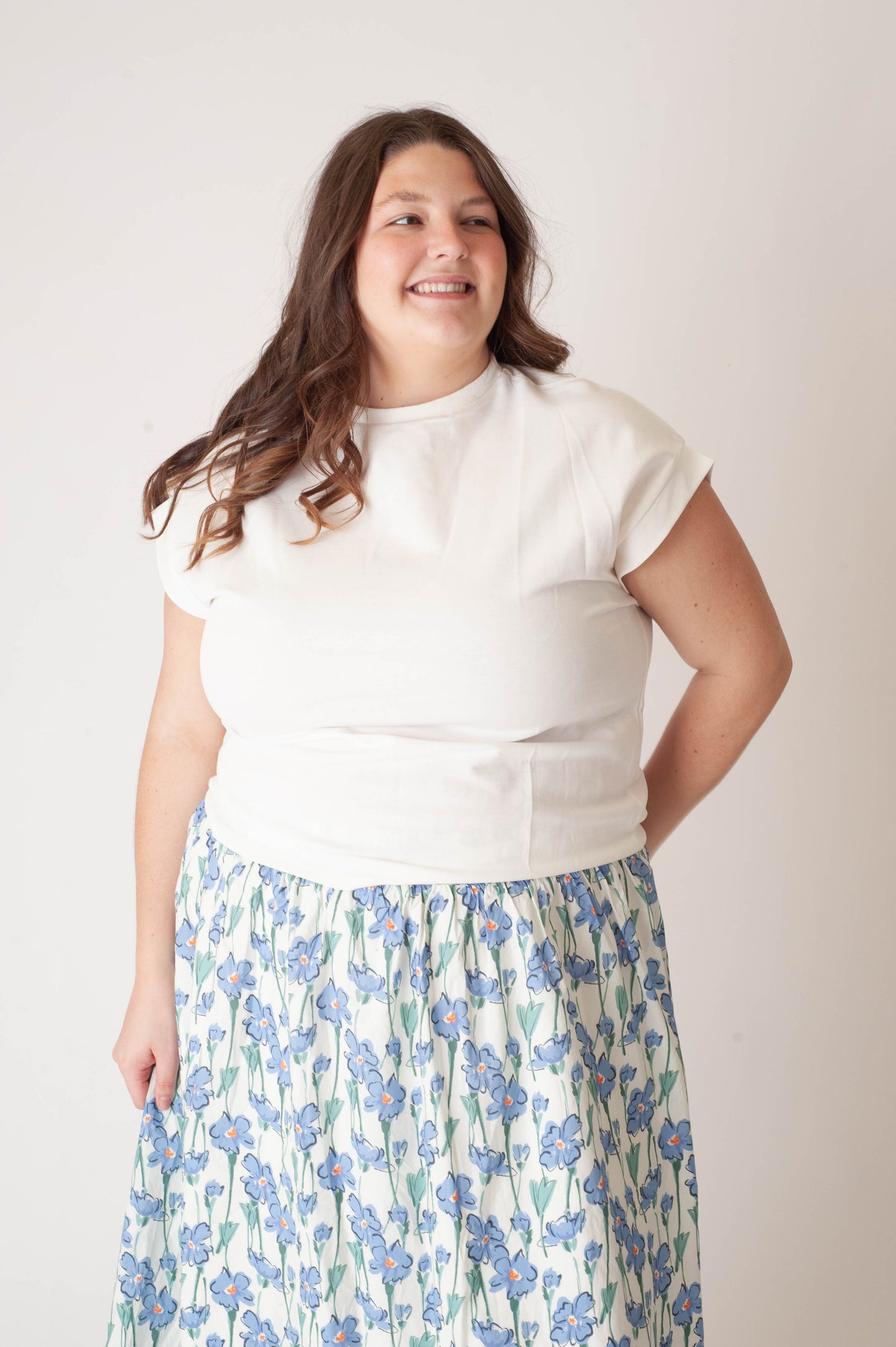 Woman wearing a white top and floral skirt against a plain background