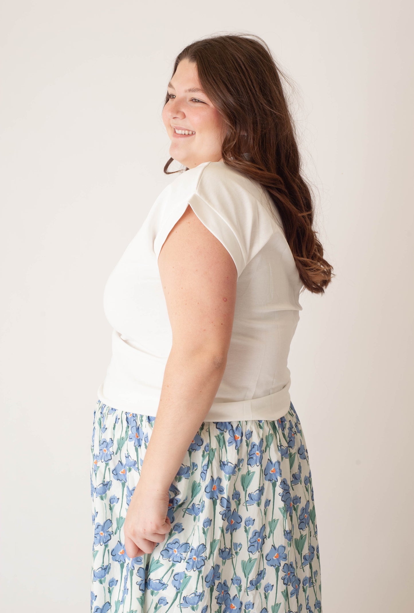 Woman wearing a white top and floral skirt against a plain background