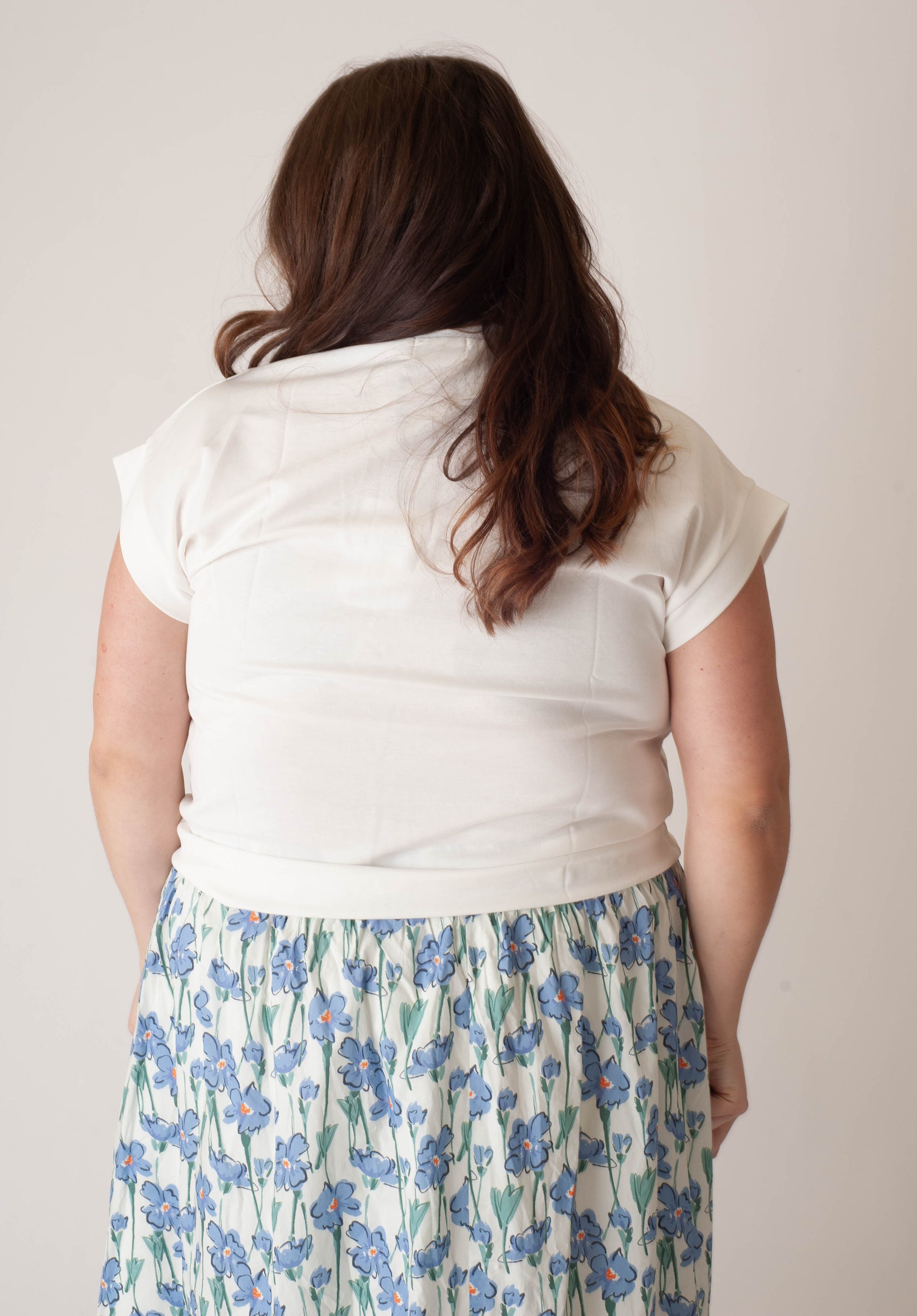 Person wearing a white top and floral skirt against a plain background