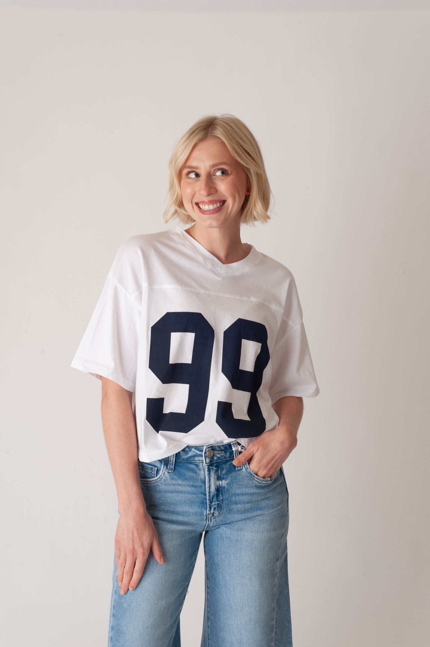 Person wearing a white t-shirt with the number 99 and blue jeans on a plain background