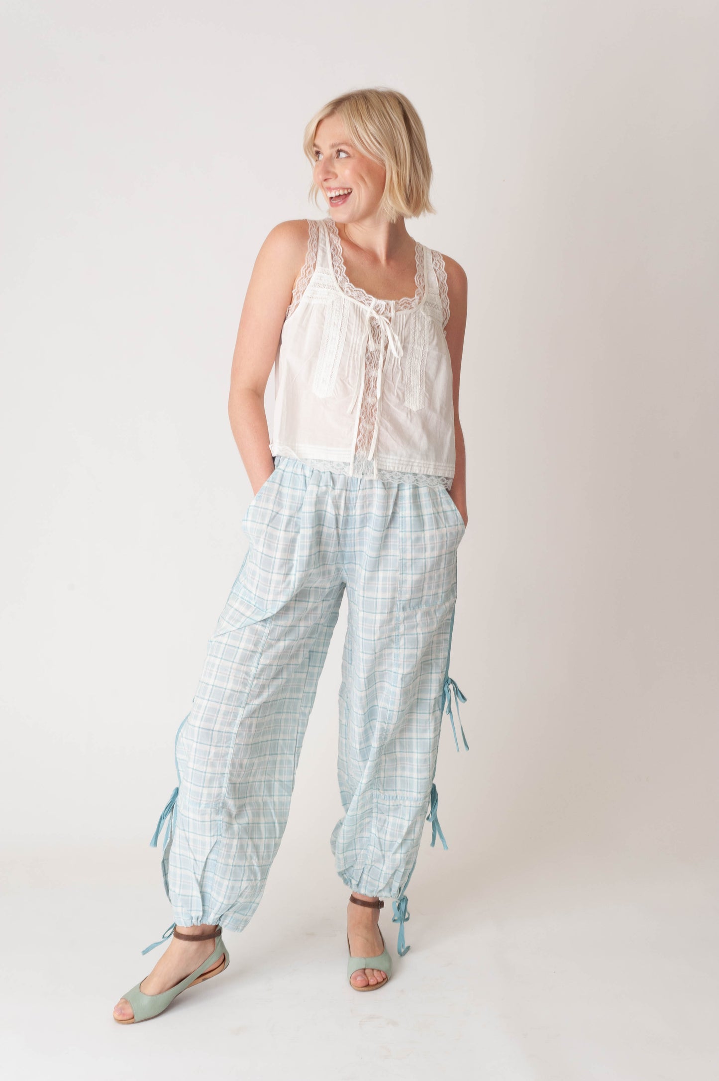 Woman wearing a white sleeveless top and light blue checkered pants on a plain background