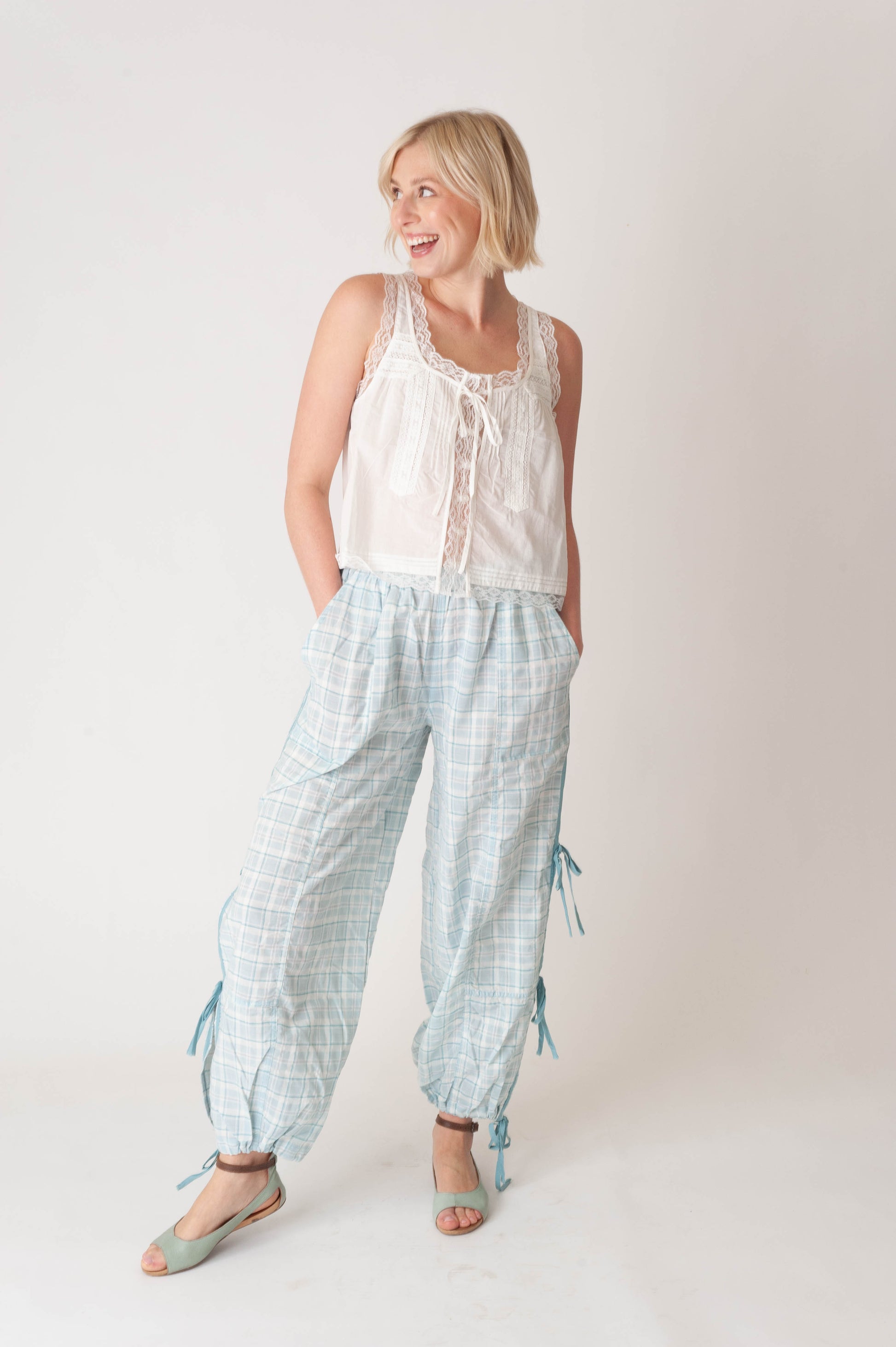 Woman wearing a white sleeveless top and light blue checkered pants on a plain background