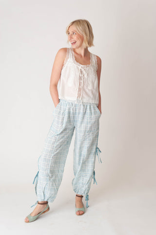 Woman wearing a white sleeveless top and light blue checkered pants on a plain background