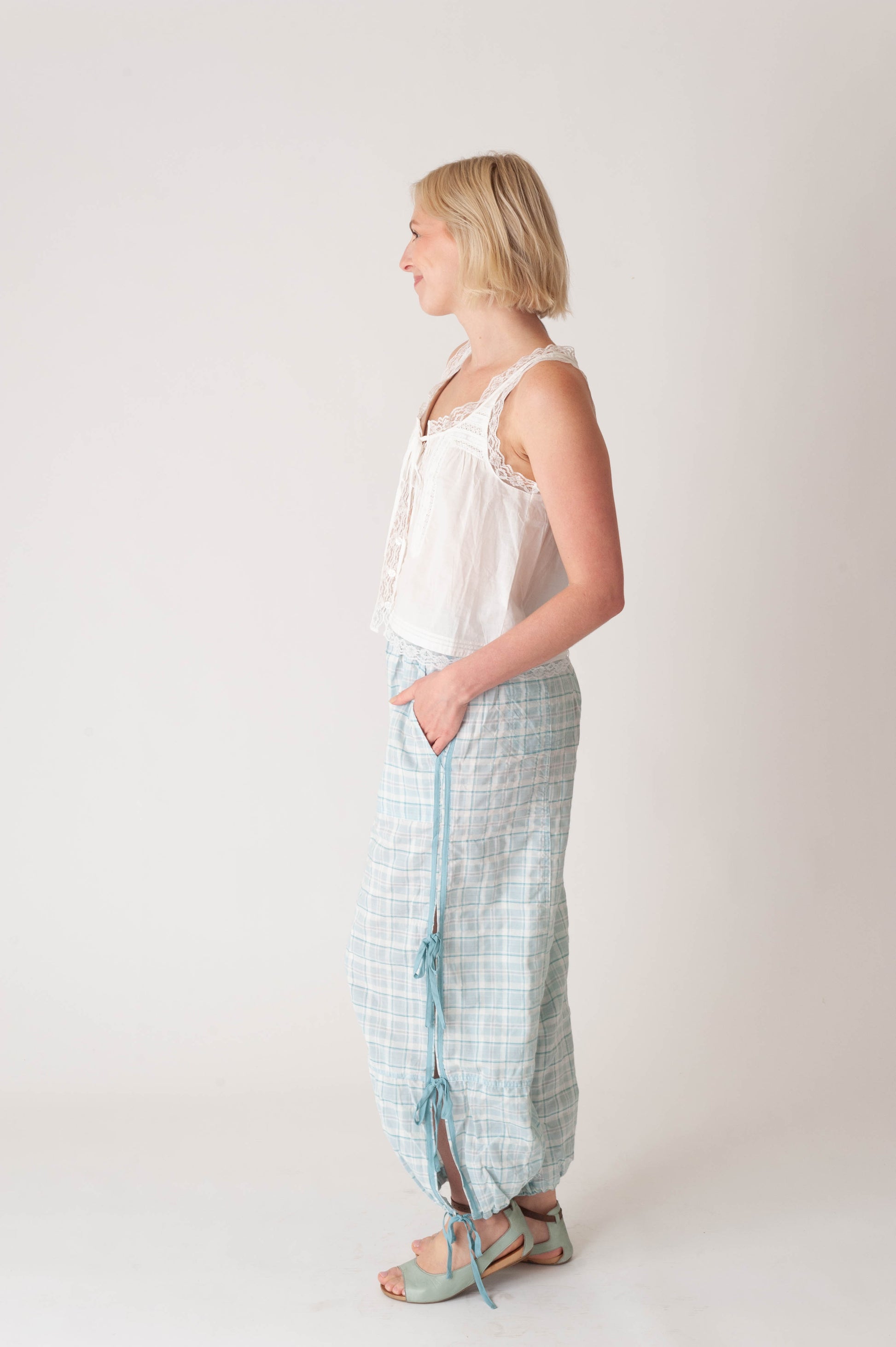 Woman wearing a white sleeveless top and light blue checkered pants on a white background