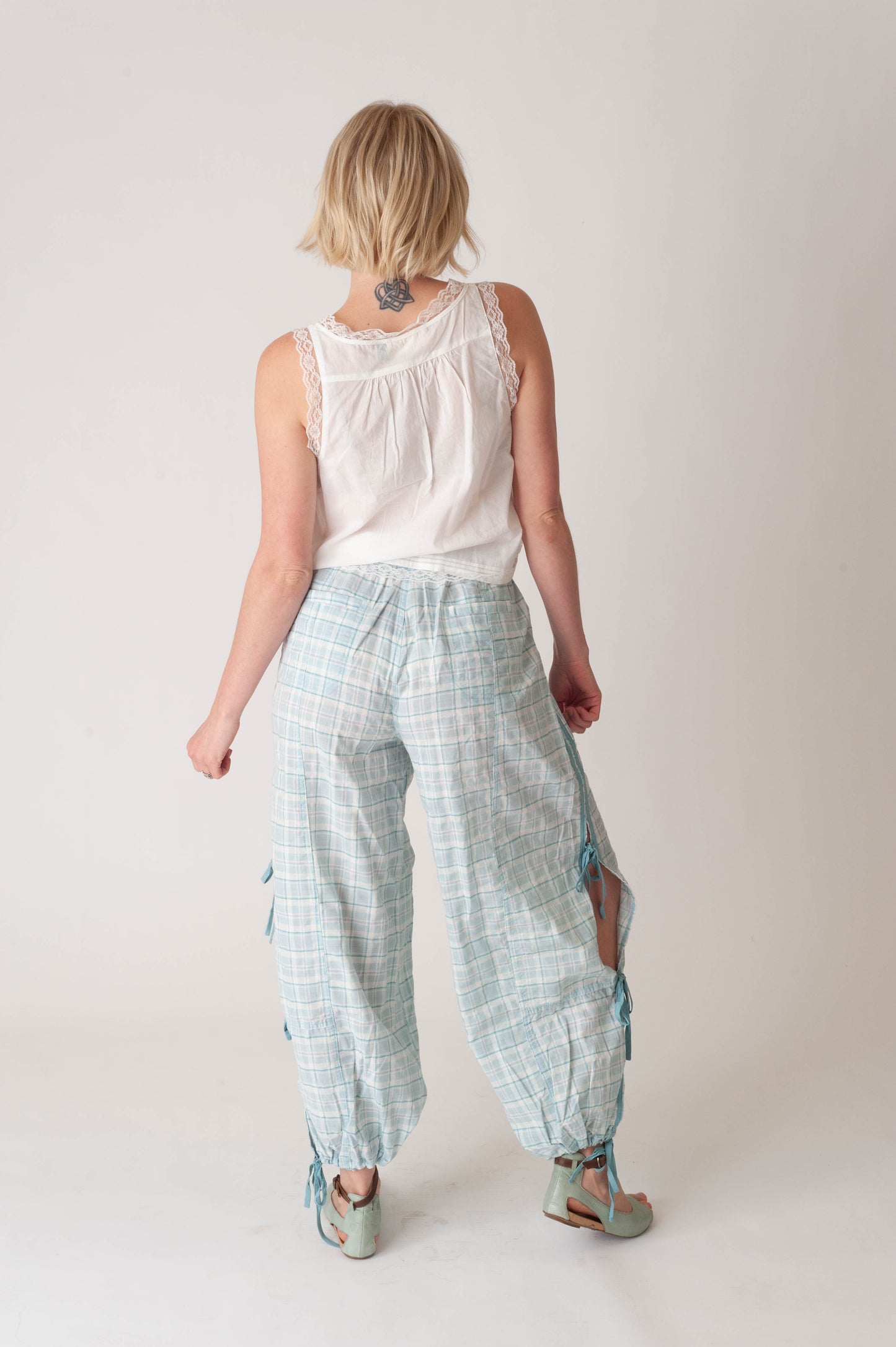 Woman wearing light blue checkered pants and a white sleeveless top on a plain background