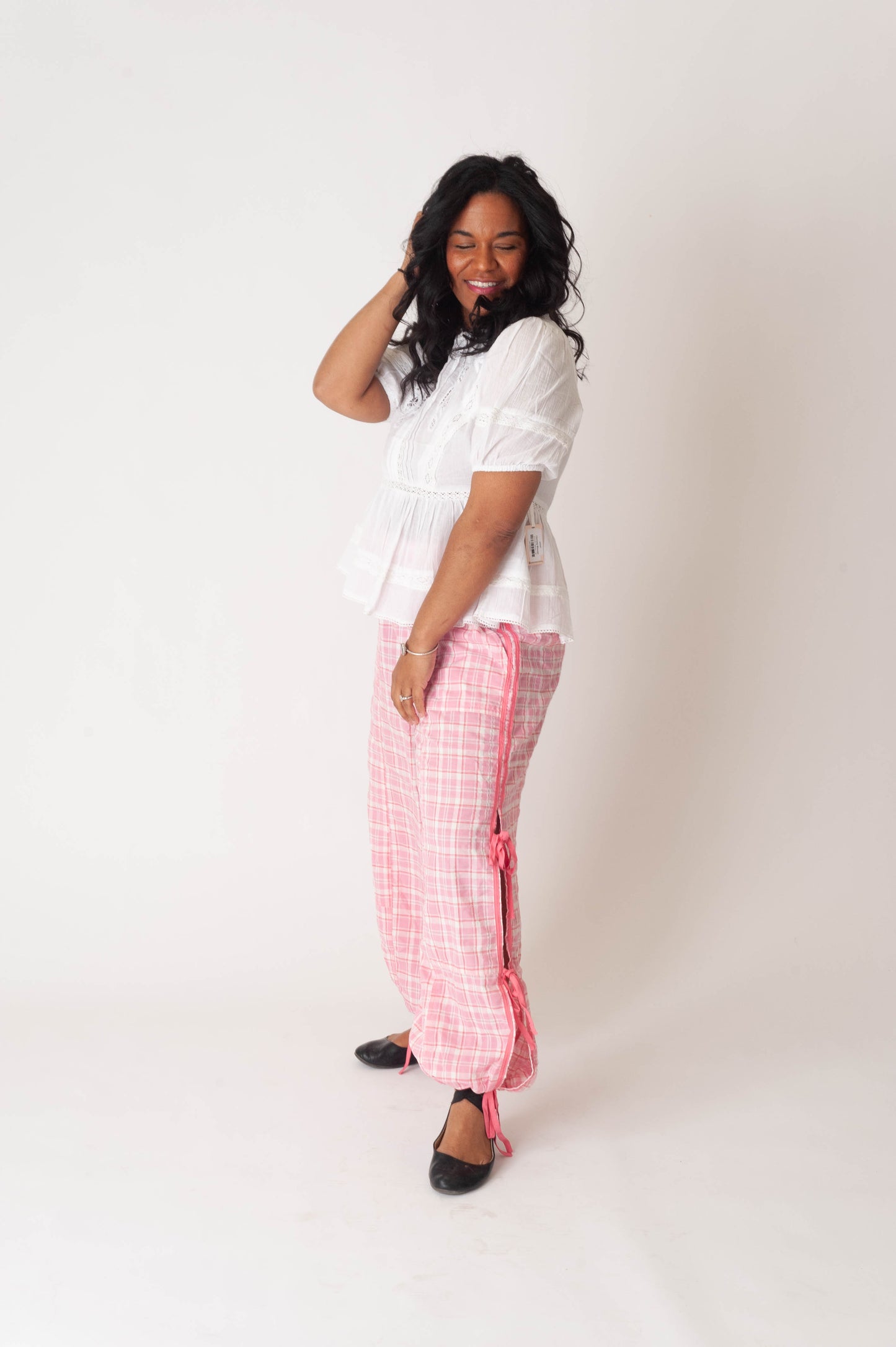 Woman wearing a white top and pink checkered pants against a white background