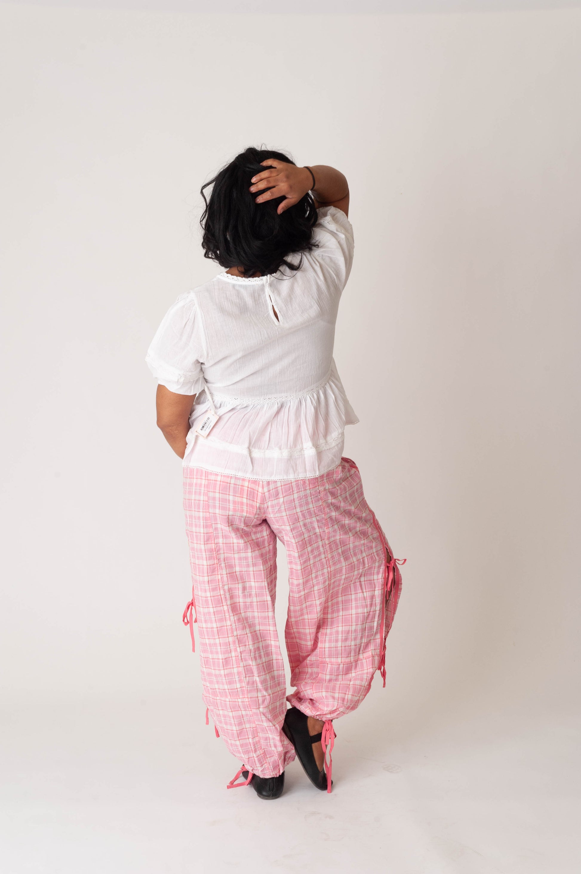 Person wearing a white top and pink checkered pants on a plain background