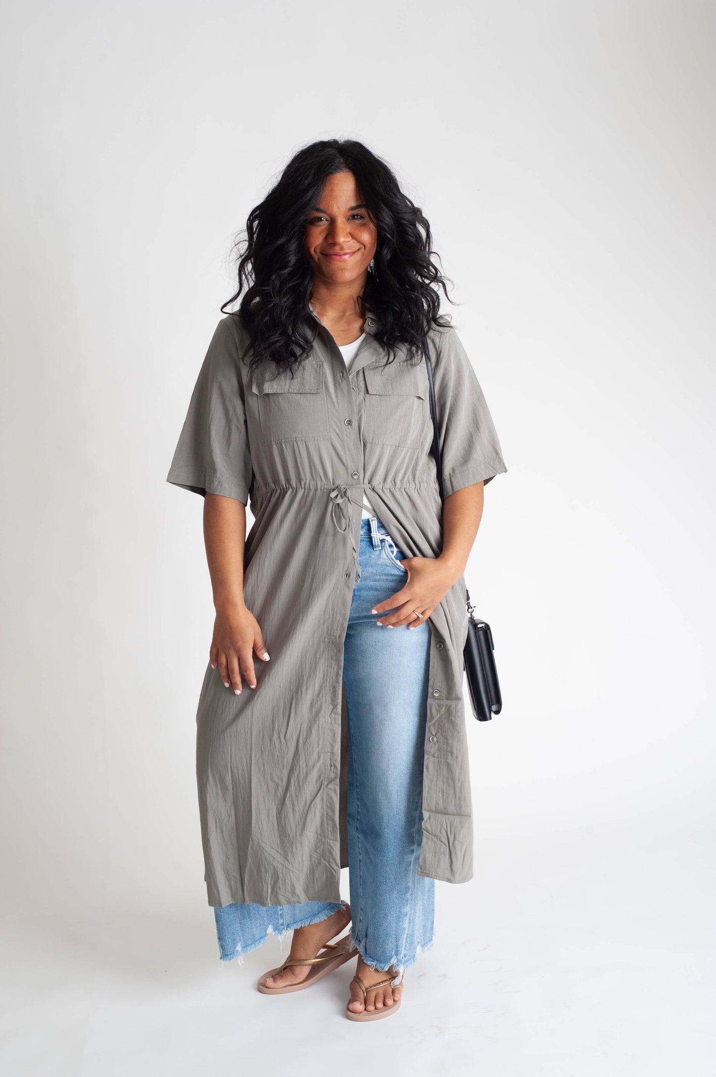 Woman wearing a long gray shirt dress over blue jeans on a white background