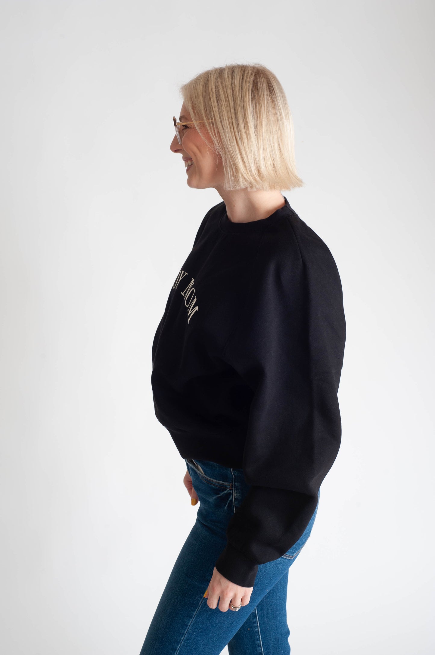 Woman wearing a black sweatshirt and blue jeans on a white background