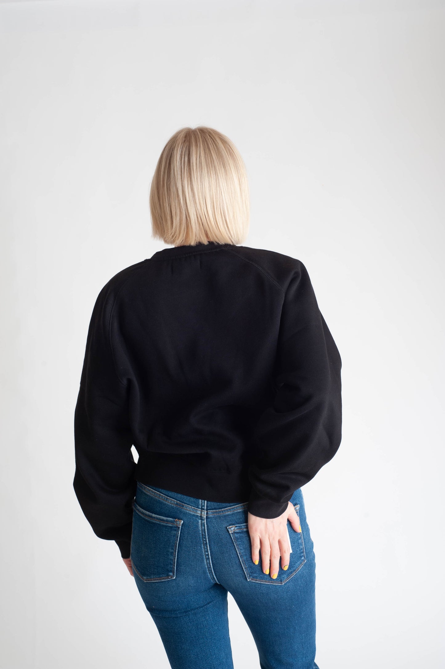 Person wearing a black sweater and blue jeans on a white background