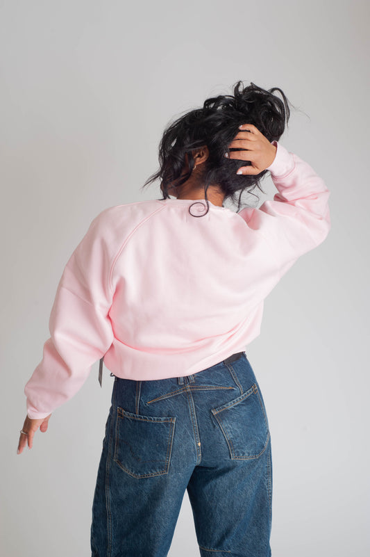 Person wearing a pink sweatshirt and blue jeans against a plain background