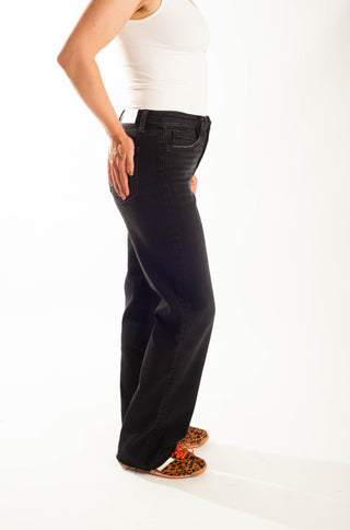 A side profile view of a person wearing black wide-leg jeans, a white tank top, and leopard print shoes against a white studio background.