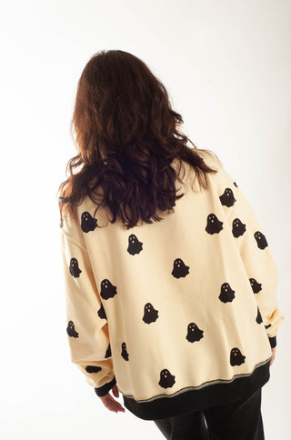 A woman viewed from behind wearing a cream-colored sweatshirt with a black ghost pattern, set against a plain white background.