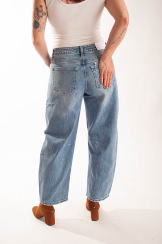 A person shown from the back wearing light-wash wide-leg denim jeans, a white tank top, and brown block-heel boots against a plain white studio background.
