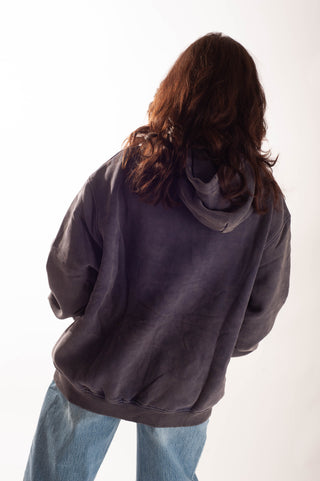 A person viewed from behind wearing an oversized faded dark gray hoodie and light blue jeans against a plain white studio background.