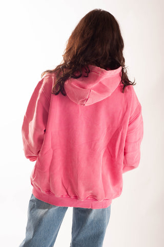 A person viewed from behind wearing an oversized pink hooded sweatshirt and light blue jeans against a plain white studio background.