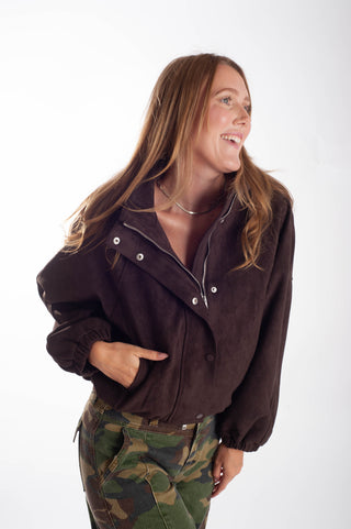 A woman wearing a dark brown corduroy jacket with silver snap details and camouflage pants, posing against a white studio background.