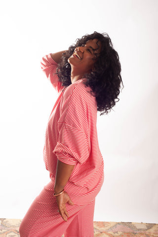 A woman with curly black hair wearing a pink and white striped long-sleeve dress, posing against a plain white studio background.