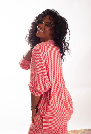 A smiling woman with curly black hair wearing a pink and white striped long-sleeve top, photographed against a plain white studio background.