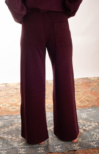 A person wearing dark navy wide-leg pants and a matching dark top, standing barefoot on a patterned rug against a plain white wall.