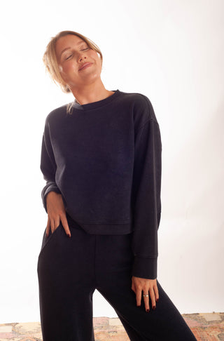A woman wearing a dark navy blue crewneck sweatshirt and matching sweatpants, posing against a bright white studio background.