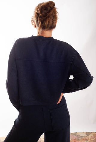 A woman shown from behind wearing a dark navy blue cropped sweatshirt and matching sweatpants against a plain white background.