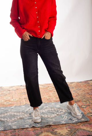 Women wearing black barrel jeans and a red cardigan against a neutral background. 