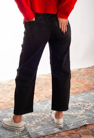 Women wearing black barrel jeans and a red cardigan against a neutral background. 