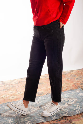 Women wearing black barrel jeans and a red cardigan against a neutral background. 