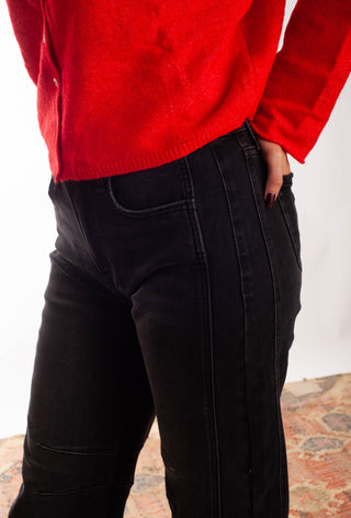 A person wearing a bright red knit sweater and black jeans, cropped from the chest down, standing against a plain light background.