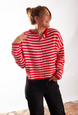 A Women wearing a striped pink and red cardigan against a white background. 