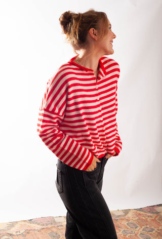 A Women wearing a striped pink and red cardigan against a white background. 
