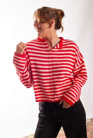 A Women wearing a striped pink and red cardigan against a white background. 