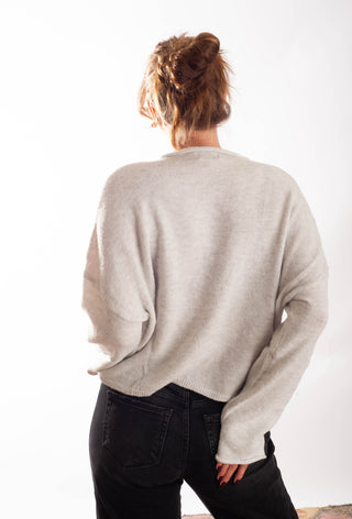 A woman viewed from behind wearing a light beige knit sweater and black jeans against a plain white background.