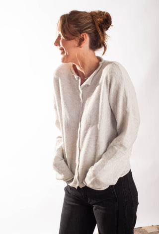 A woman wearing a light beige knit button-up shirt with black pants, standing against a plain white background.