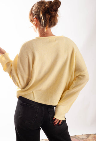 A woman shown from behind wearing a pale yellow knit sweater and black jeans against a plain white background.