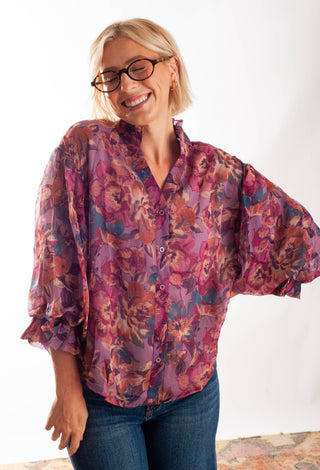 A women wearing a floral blouse with a button up front against a white background. 