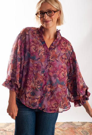 A women wearing a floral blouse with a button up front against a white background. 