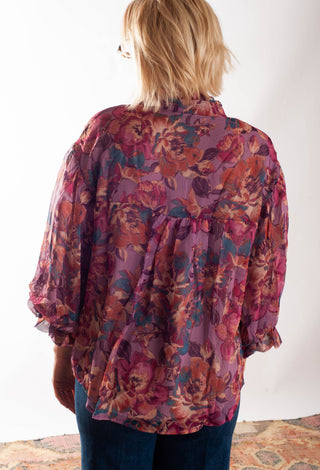 A women wearing a floral blouse with a button up front against a white background. 
