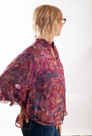 A women wearing a floral blouse with a button up front against a white background. 
