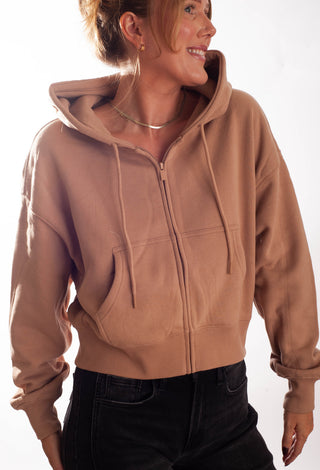 A woman wearing a cropped, zip-up hoodie with black jeans, standing against a plain white studio background.
