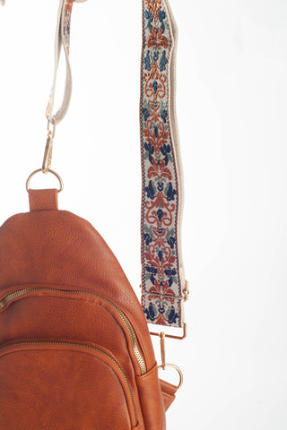 Close-up of a brown faux-leather crossbody bag with a patterned woven strap featuring blue, rust, and cream motifs, shown against a white background.