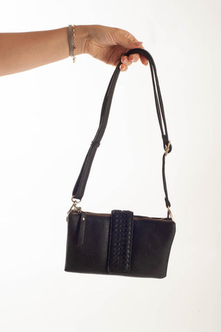 A black leather shoulder bag with a braided front detail and gold-tone hardware, held by a person's hand against a plain white background.