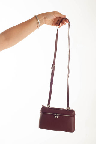 A burgundy leather shoulder bag with a silver-tone butterfly clasp and a matching long strap, held by a person's hand against a plain white background.